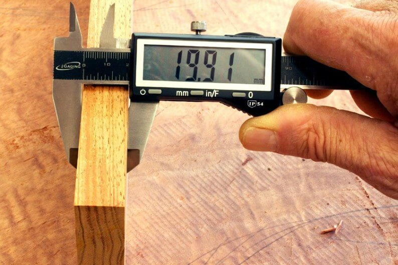 Na imagem, uma pessoa utilizando um paquímetro para medir um pedaço de madeira